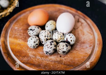 quaglia e gallina uova marroni e bianche sul piatto di legno e sfondo nero Foto Stock