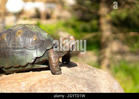 Scultura di una tartaruga. Tartaruga di bronzo su una pietra. La figurina adorna il parco. Scultura di una tartaruga alla luce del sole. Foto Stock