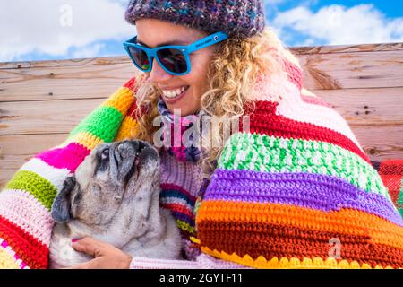 Giovane donna che abbraccia il suo cane mentre si rilassa a letto contro il cielo. Primo piano di donna e il suo cane pug in abiti invernali. Donna felice con animale domestico godere Foto Stock