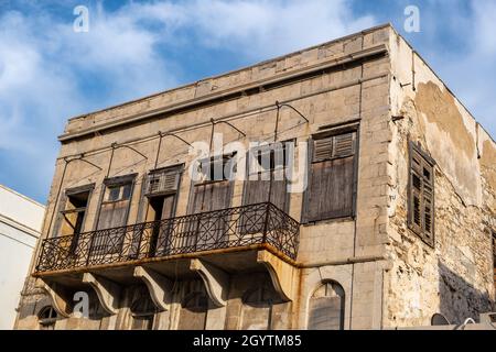 Parte di danneggiato scalpellino casa sbucciata invecchiata abbandonata con persiane di legno rotto chiuso ringhiere balcone arrugginito a Ermoupoli capitale dell'isola di Syros C. Foto Stock