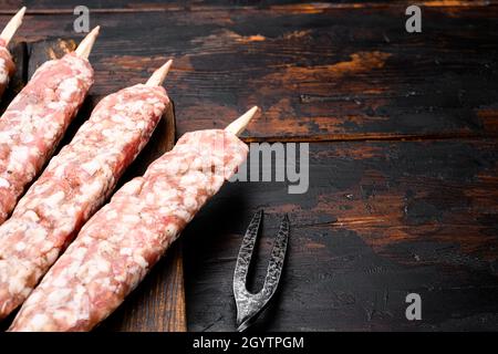 Salsicce di manzo crudo e di agnello con kebabs, adagiato su un vecchio sfondo di legno scuro, con spazio per la copia del testo Foto Stock