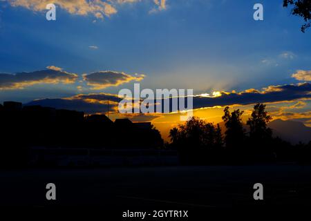 Tramonto urbano sugli alberi in una serata nuvolosa Foto Stock