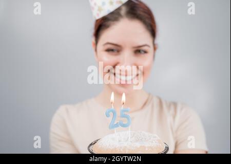 La donna felice fa un desiderio e soffia fuori le candele sulla torta di 25 compleanno. Ragazza che festeggia il compleanno. Foto Stock