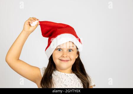 Primo piano ritratto di ragazza maliziosa e giocosa in rosso Santa Hat che tiene pompom con mano, isolato su sfondo bianco con spazio copia Foto Stock