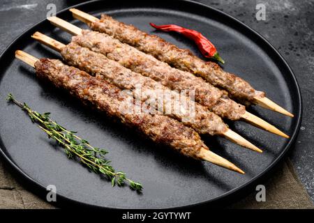 Sgranate il kebab su un bastone, dalla terra macinata di carne di montone, sul piatto, su sfondo nero di tavola di pietra scura Foto Stock