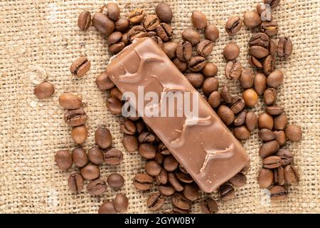 Una barra di cioccolato con chicchi di caffè, primo piano, sul burlap, vista dall'alto. Foto Stock