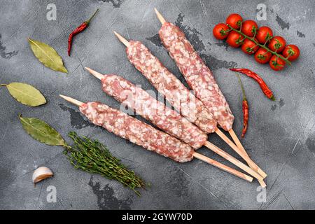 Salsicce di carne di manzo crudo e di agnello, con ingredienti alla griglia, su sfondo tavola di pietra grigia, vista dall'alto piatto Foto Stock