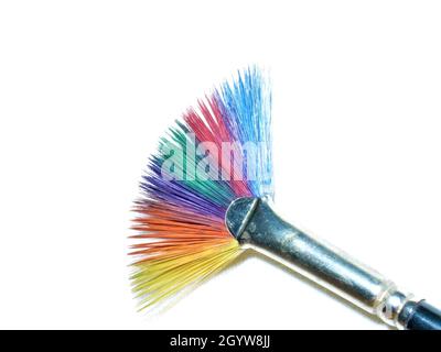 Primo piano di un pennello dipinto in colori arcobaleno su sfondo bianco di tela. Foto Stock