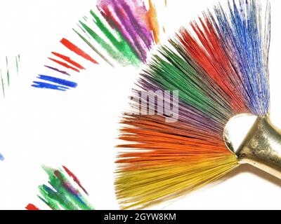 Primo piano di un pennello dipinto in colori arcobaleno su uno sfondo bianco con pennellate colorate. Foto Stock