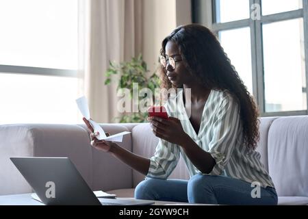 Giovane donna nera in possesso di carta che paga le fatture in applicazione mobile sul cellulare. Foto Stock
