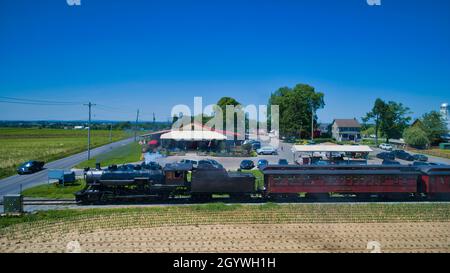 Vista aerea di un treno a vapore Puffing Smoke e vapore che passa persone in un Motel che passa attraverso le Farmlands Foto Stock
