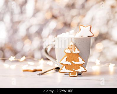 Albero e stelle biscotti Gingerbread con una tazza di cioccolata calda e marshmallows su un caldo bokeh luci di Natale sfondo. Foto Stock