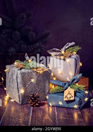 Tre confezioni regalo ecologico in stile furoshiki, confezionate su sfondo scuro e illuminate. Zero rifiuti di Natale riciclaggio, riutilizzo, stile di vita sostenibile conce Foto Stock