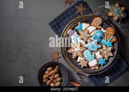 Biscotti natalizi decorati con pan di zenzero ghiacciato bianco e blu su un piatto rustico con spezie. Sfondo grigio scuro. Vista dall'alto con spazio di copia Foto Stock