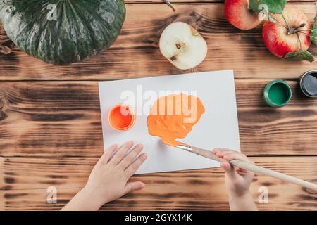 Passo-per-passo Halloween bambini tutorial stampe di mela zucca. Fase 5: Le mani dei bambini spennellano la vernice arancione del gouache sulla carta. Vista dall'alto Foto Stock