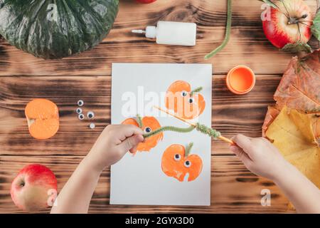Passo-per-passo Halloween bambini tutorial stampe di mela zucca. Passo 14: La mano del bambino avvolge il filo soffice verde intorno alla matita. Vista dall'alto Foto Stock