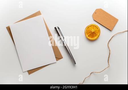 Biglietto di auguri natalizio con etichetta regalo busta artigianale, penna stilografica e una fetta di arancia secca su una scrivania bianca pulita. Foto Stock