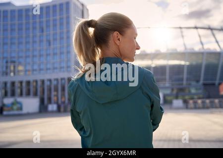 Vista posteriore di una donna sportiva di mezza età in abbigliamento sportivo in piedi all'aperto, pronta per l'allenamento mattutino Foto Stock