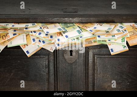 Antico petto di legno da cui fuoriescono bollette in euro. Risparmio, denaro nero, contanti, flusso di cassa. Foto Stock