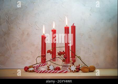 Quattro candele rosse, tre sono accese per la terza Domenica prima di Natale, decorazione dell'Avvento su un tavolo di legno contro una parete rustica, spazio copia, selezionato Foto Stock