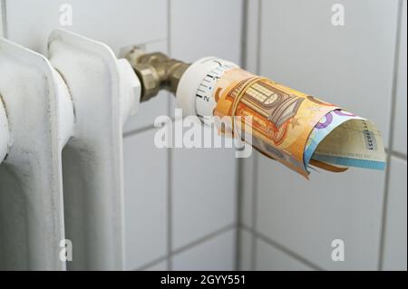 Termostato su un vecchio radiatore avvolto con banconote in euro, concetto per l'aumento dei costi di calore ed energia in un inverno freddo, fuoco selezionato, profondità stretta o Foto Stock