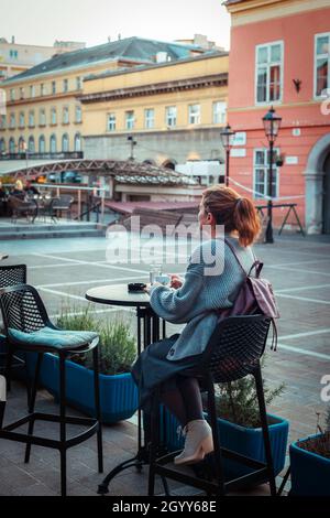 Ragazza che beve caffè a un tavolo in un caffè di strada. Foto Stock