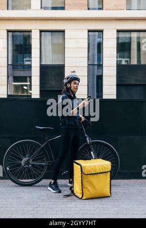 Corriere donna in uniforme in piedi in città con smartphone che controlla l'indirizzo del cliente Foto Stock