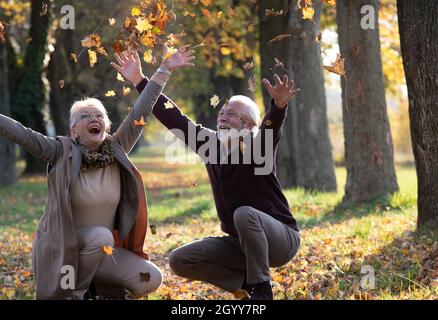 Felice coppia senior gettando le foglie nel parco in autunno in giorno di sole Foto Stock
