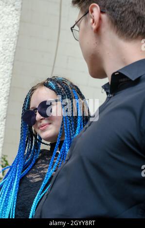 Una donna flirta con un giovane uomo. Giovane donna con dreadlock blu con occhiali da sole. Il maschio è in piedi accanto a lei. Porte d'ingresso. Messa a fuoco selettiva. Foto Stock