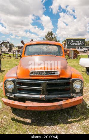 Vista frontale di un vecchio camion studebaker arancione arrugginito parcheggiato in un terreno erboso con un cielo blu e nuvole sullo sfondo Foto Stock