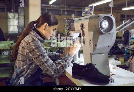 Giovane donna che utilizza una macchina da cucire industriale presso l'officina di una fabbrica di calzature Foto Stock