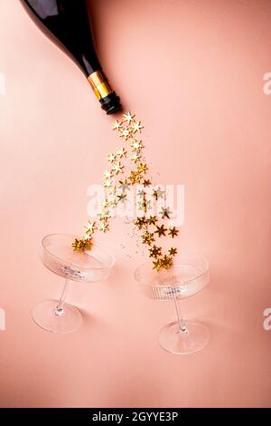 Bottiglia di champagne con spruzzi dorati scintillanti e bicchieri di champagne su sfondo rosa. Disposizione piatta, vista dall'alto, stile natalizio alla moda. Foto Stock