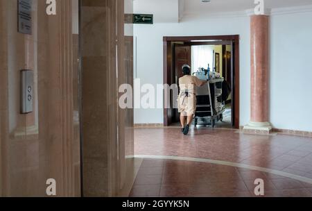 La cameriera spinge il carrello lungo il corridoio dell'hotel. Cameriera al lavoro e filobus con servizio in camera e attrezzature per la pulizia in hotel Foto Stock