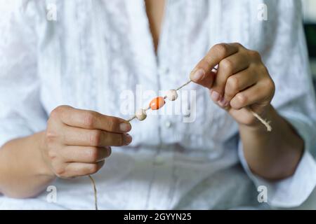 Primo piano sulla sezione centrale di sconosciuto femmina stringa di tenuta con perle di legno o plastica che fanno natura materiali collana bracciale a casa - Creative des Foto Stock