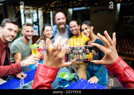 Le mani femminili scattano foto con il telefono cellulare di giovani amici al pub alla moda Foto Stock