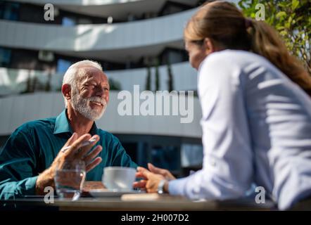 Uomo maturo felice seduto caffè con giovane donna d'affari e chiacchierare Foto Stock