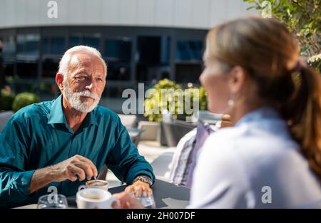 Uomo maturo felice seduto caffè con giovane donna d'affari e chiacchierare Foto Stock