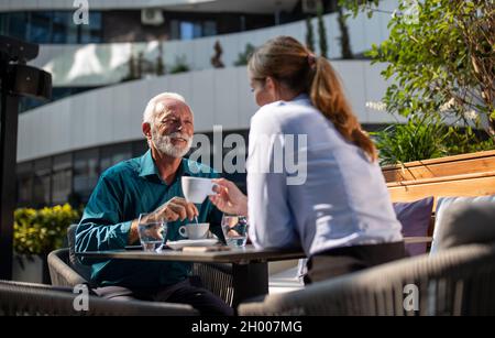 Uomo maturo felice seduto caffè con giovane donna d'affari e chiacchierare Foto Stock