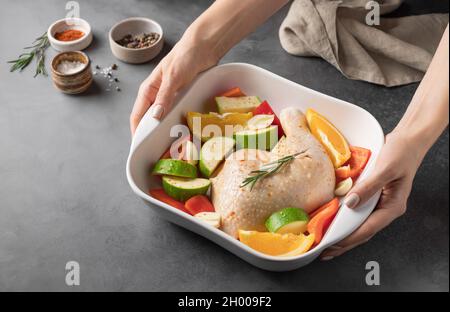 le mani femminili tengono una teglia in ceramica con carne di pollo cruda Foto Stock