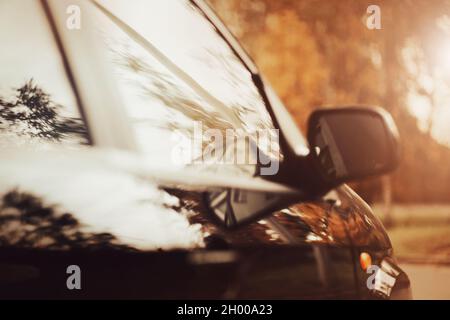 Un'immagine sfocata di un'auto nera che guida velocemente in una giornata di sole autunnale sulla strada, nelle finestre di cui i rami di alberi sono riflessi. Un viaggio a. Foto Stock