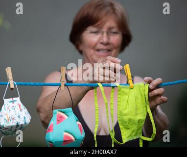 Donna anziana lavaggio e asciugando le maschere di sicurezza di stoffa su appendiabiti in giardino durante la quarantena. Virus e responsabilità pandemica e concetto di auto-cura Foto Stock