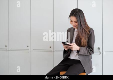 Donna che lavora allegra usando il telefono cellulare sorridendo con piacere mentre legge un messaggio di testo in ufficio Foto Stock