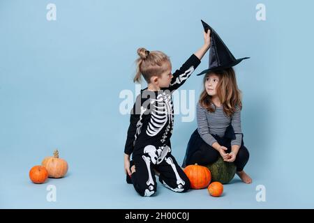 Ragazzo in costume di scheletro togliendo un cappello di strega da una ragazza, lo guarda. Sono vestiti per Halloween. Su sfondo blu. Foto Stock