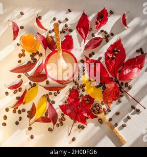 Tazza di caffè caldo in chicchi di caffè torrefatto e foglie d'autunno rosse e gialle su un tavolo Foto Stock