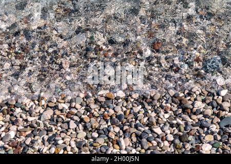 Ciottoli bagnati di piccolo colore sulla riva del mare. Vista ravvicinata dall'alto. Trama, sfondo, sfondo. Foto Stock