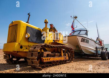 Un trattore attrice una barca da pesca dal mare sul lungomare di Hastings nel Sussex orientale, Inghilterra Foto Stock