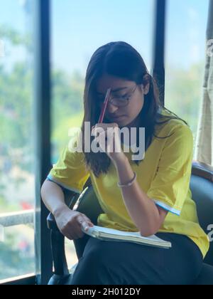 Una ragazza in scrittura di pensiero profondo su un blocco note. India. Foto Stock