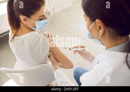 La giovane donna che indossa una maschera medica sta ricevendo un'iniezione di vaccino nel suo braccio Foto Stock