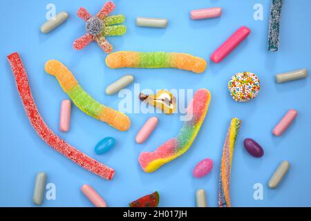 Dolci di diverse forme e colori su sfondo blu. Caramelle in gelatina e vista dall'alto della tasca. Molti dolci diversi sfondo. Foto Stock