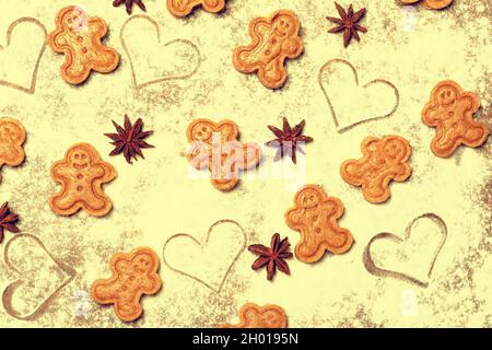 Un colorato motivo felice fatto di biscotti di pan di zenzero, frutti di anice stellato e simboli di cuore disegnati sul piano di lavoro della cucina cosparso di farina. Foto Stock